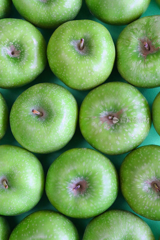 一组绿色的史密斯苹果(Malus domestica)的全画幅图像，有茎，光滑，有斑点的果皮，绿色背景，高架视图